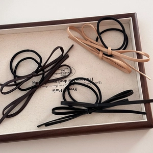 Élastiques à cheveux avec nœud en cuir en noir, marron et kaki sur un plateau en lin