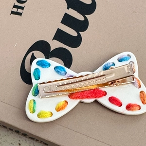Vista dettagliata del bordo ricamato multicolore sul fermaglio a fiocco bianco con clip dorata