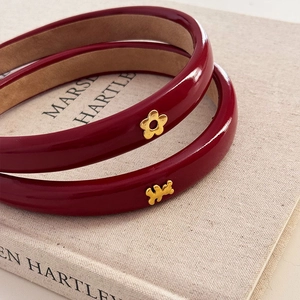 Détail de serre-têtes en cuir verni rouge avec breloques fleurs et ours dorées