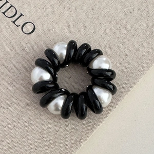 Détail d'élastique cheveux spirale noir avec perles blanches sur toile grise texturée