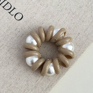 Gros plan sur élastique spirale kaki avec grandes perles blanches sur fond en toile