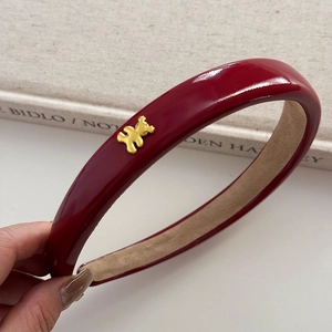 Détail d'un serre-tête en cuir verni rouge avec breloque d'ours doré et doublure douce
