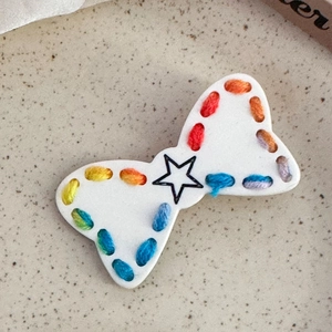Dettaglio macro di un fermaglio a fiocco con cuciture arcobaleno e stella nera