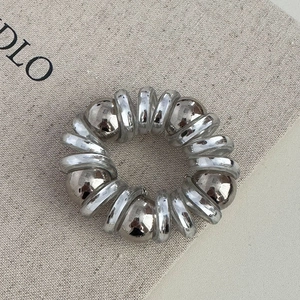 Détail d'élastique spirale argenté avec perles métalliques sur fond en toile
