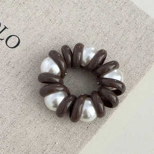 Détail d'un chouchou spirale marron café avec perles sur tissu beige texturé