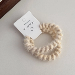 Close-up of two beige fuzzy elastic hair ties with soft faux fur texture on display card
