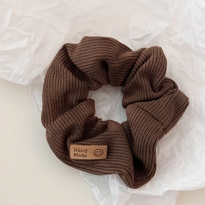 Detail of dark brown knitted scrunchie with a handmade smile patch on white texture