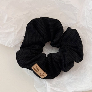 Close-up of black knitted hair scrunchie featuring a handmade smiley face woven label