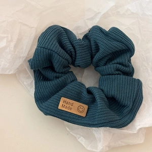 Deep teal knitted scrunchie with a brown handmade smiley face patch for hair styling