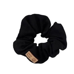Black knitted scrunchie with vertical ribbed texture and brown smiley handmade label