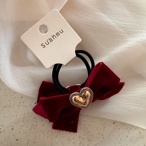 Dettaglio dell'elastico per capelli in velluto rosso scuro con cuore d'oro su carta bianca