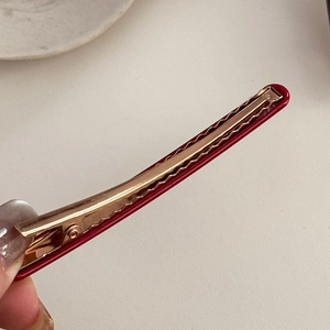 Détail d'une pince à cheveux en acétate rouge avec base en métal doré rose pour un maintien sûr