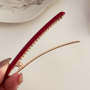 Vue détaillée d'une pince à cheveux en acétate rouge avec dents dorées et design ouvert