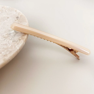 Gros plan sur une barrette en acétate avec base en métal or rose sur marbre