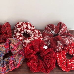 Macro view of 6 red festive tweed and houndstooth scrunchies on a wooden display