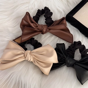 Trois chouchous nœuds en cuir marron, beige et noir posés sur un fond en fourrure blanche