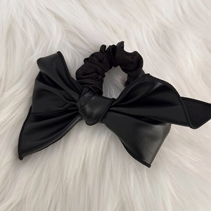 Détail d'un chouchou en cuir PU noir avec grand nœud sur un fond en peluche blanche