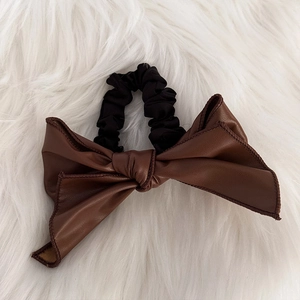 Détail d'un chouchou noeud en simili cuir marron foncé avec texture sur fond de fourrure