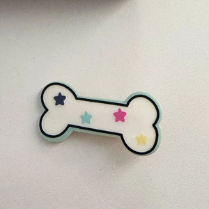 Dettaglio di un fermaglio per capelli a forma di osso con stelle colorate e base verde