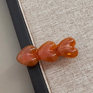 Detailansicht der bernsteinfarbenen Acetat-Haarspange mit drei Herzen und goldenem Text