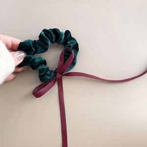 Detailansicht eines dunkelgrünen Samt-Scrunchies mit rot-schwarzer gestreifter Bandschleife