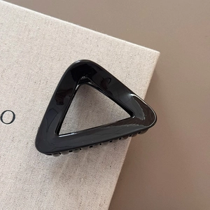 Detail of a glossy black triangular hair claw clip with metal spring on a textured book