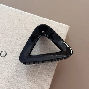 Polished black triangular hair claw clip detail with glossy finish on a cream background