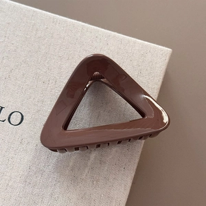 Detail view of a glossy dark brown triangular hair claw clip on a beige textured gift box