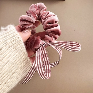 Detail von rosa Samt-Haargummi mit karierter Schleife vor einem beigen Strickpullover