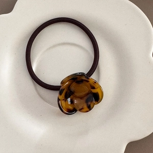 Macro detail of tortoiseshell camellia flower resin hair ring on white ceramic plate