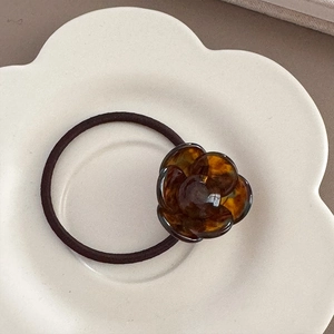 Close-up of tortoise shell resin flower elastic hair tie on a white ceramic tray