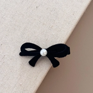Gros plan d'une barrette nœud en velours noir avec perle blanche sur un tissu texturé élégant
