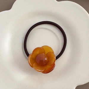 Detailed view of an amber acetate flower elastic hair tie on a white petal tray