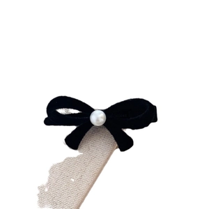 Barrette nœud en velours noir élégante avec perle blanche sur fond de lin rustique