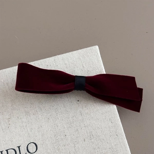 Detail of burgundy velvet bow hair clip with black ribbon knot on a neutral background