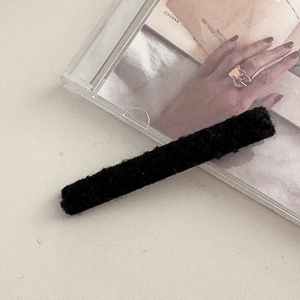 Dettaglio di un fermaglio per capelli in lana nera su uno sfondo dal design minimal