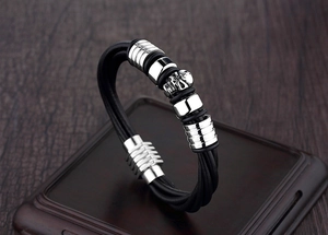 Close-up of punk leather bracelet with raven skull charm and metallic striped rings