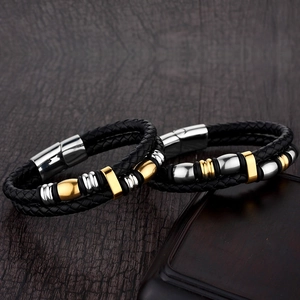 Detail view of woven black leather bracelet with silver and gold metal charms on wood