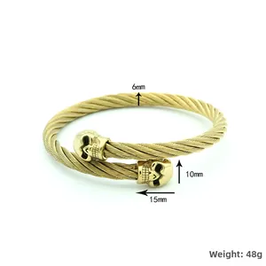 Detalle de pulsera de cable de acero dorado de 6mm con dijes de calavera y peso de 48g