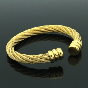 Vista macro de pulsera rígida de cable trenzado dorado con puntas cilíndricas de tres anillos