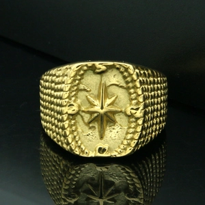 Macro detail of men's gold signet ring featuring compass star relief and rope textures