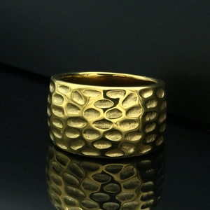 Detailed macro shot of a gold wide band ring with a unique hammered texture on black background