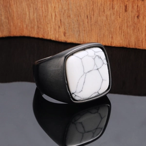 Macro shot of men's matte black steel ring with white marble stone on dark surface