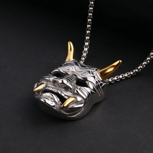 Macro shot of silver and gold Hannya mask pendant showing detailed metal textures and engravings