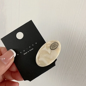 Detail of oval acetate hair clip with POKO FOSCA metal logo plate on cream marble resin