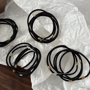 Close-up of high-elastic black hair ties with elegant gold metal beads on white paper