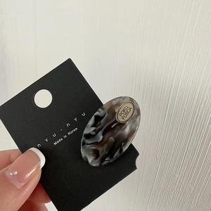 Close-up of oval marble pattern acetate hair clip with metal plate on black card