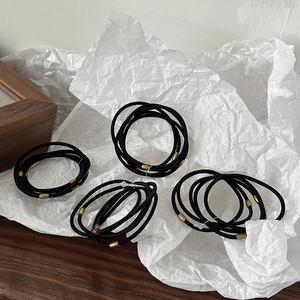 Detail of high-elasticity black hair ties with golden metal cylinders on a textured surface