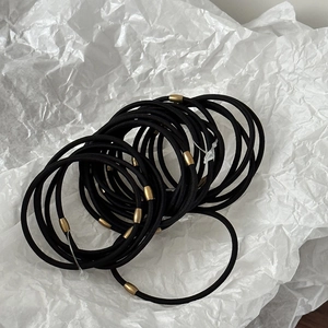 Five slim elastic hair ties with gold metal buckles on a white paper background