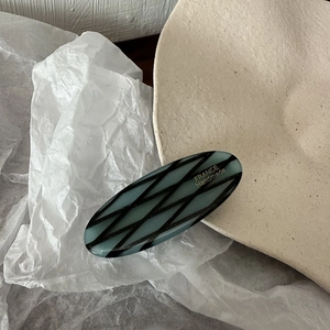 Macro detail of oval acetate hair clip in grey-blue with black grid and France Handmade logo